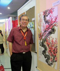 Eng'r Felix Chan Lim poses beside the painting of a plum tree. It's a painting he and brother Alex made. Felix painted the trunk, Alex painted the flowers and the calligraphy.