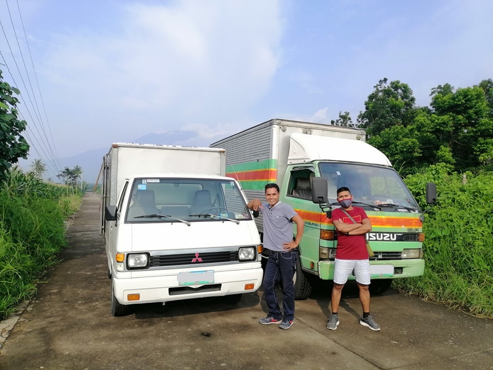 two men pose by an isuzu elf and a smaller container van